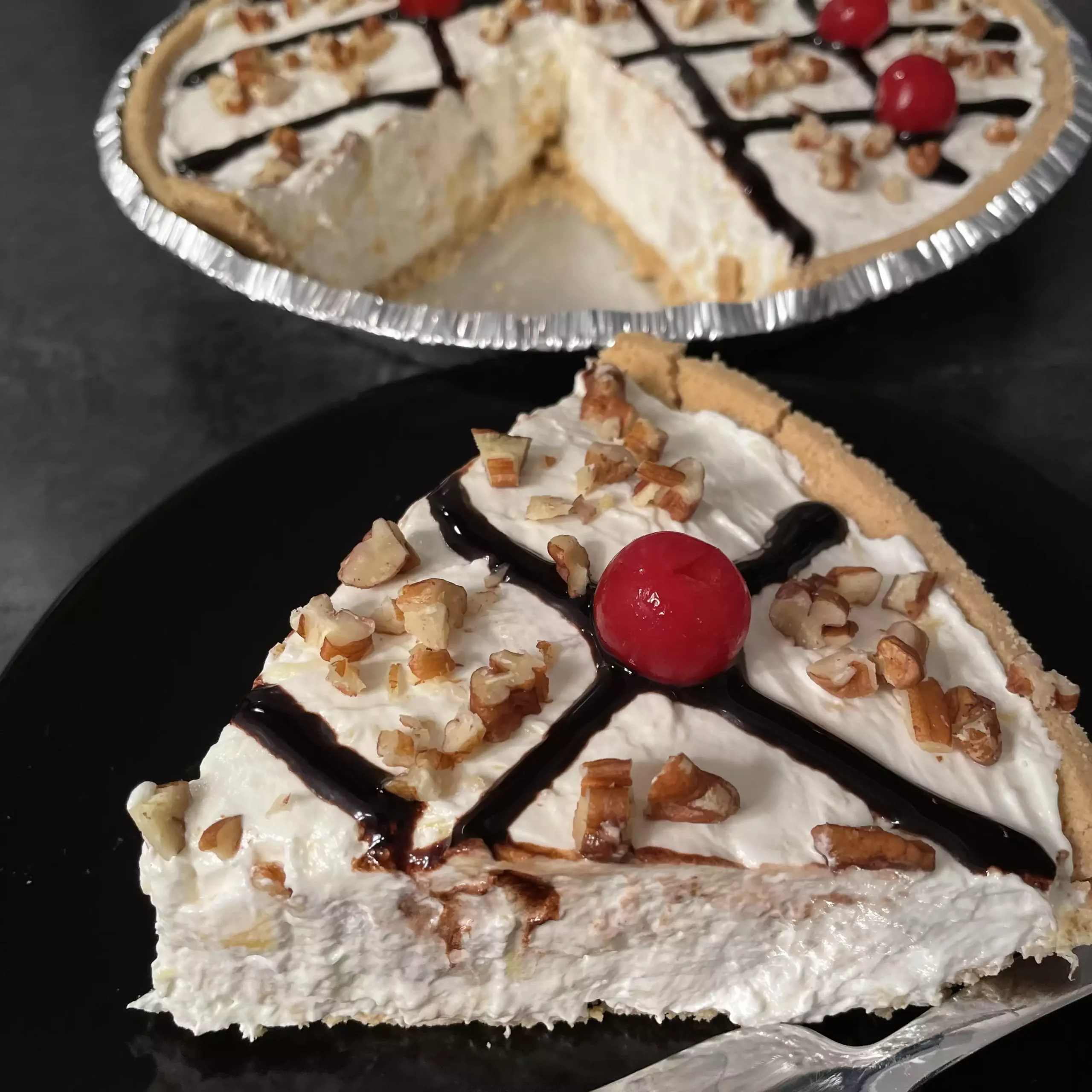 Banana Split Pie topped with whipped cream, cherries, and pecans on a graham cracker crust.